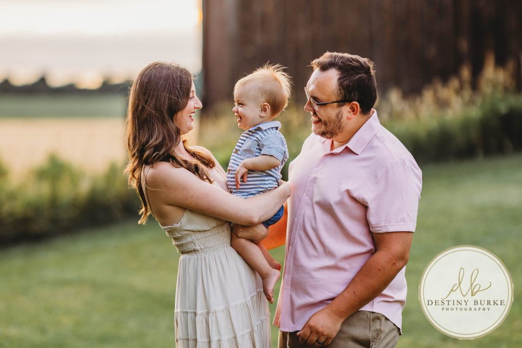 Golden hour extended family photo of the Carson/Ingersoll family in Caledonia, NY, featuring parents, grandparents, and their smiling young child. Captured by Destiny Burke Photography with warm light, candid emotion, and timeless connection.